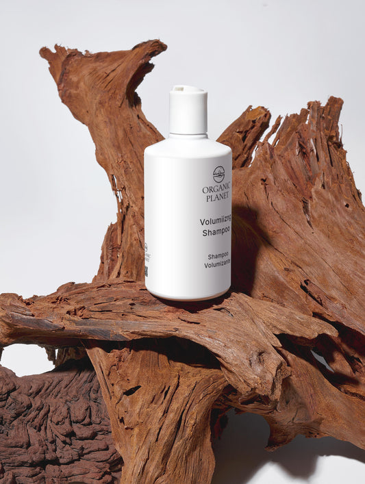 White shampoo bottle labeled 'Organic Plant' on a wooden surface. Nourish and Volumize Shampoo thoroughly cleanses hair while maintaining its softness. It strengthens each strand and adds noticeable volume with the help of Hydrolysed Wheat Protein. Hydrating ingredients such as Glycerin, Betaine, and Xylitol deeply condition and nourish the hair. Mild surfactants like Sodium Coco-Sulfate, Coco-Glucoside, and Cocamidopropyl Betaine deliver effective cleansing, while Brassica Alcohol and Brassicyl Isoleucinat