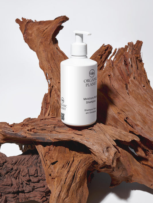 White shampoo bottle labeled 'Organic Planet' on a wooden surface. This vegan shampoo gently cleans and moisturizes hair using organic Aloe Vera and botanical extracts. Free from sulfates, parabens, and silicones, it is ECOCERT COSMOS certified and comes in eco-friendly packaging. It leaves hair soft, smooth, and full of volume while supporting sustainable beauty.